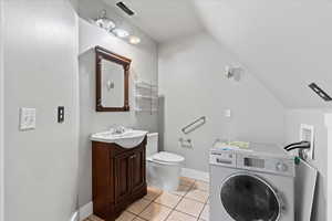Bathroom featuring washer / dryer, vanity, vaulted ceiling, and tile patterned flooring