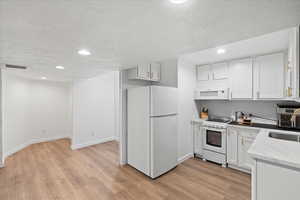 Kitchen with white appliances, recessed lighting, a textured ceiling, light wood-style flooring, and white cabinets