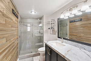 Full bath with vanity, a stall shower, and wood walls
