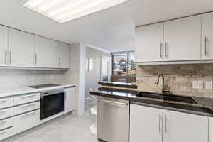 Kitchen with appliances with stainless steel finishes, decorative backsplash, light marble finish floors, ornamental molding, and white cabinetry