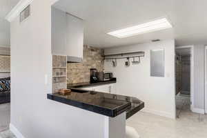 Kitchen with stainless steel microwave, dark countertops, backsplash, white cabinetry, and a peninsula