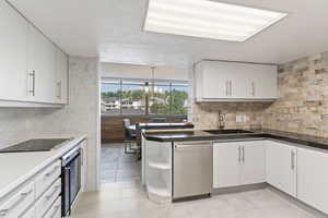 Kitchen featuring stainless steel dishwasher, black electric cooktop, wine cooler, white cabinets, and open shelves