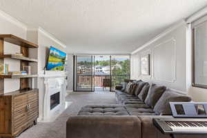 Carpeted living room with a textured ceiling, crown molding, a fireplace with flush hearth, and floor to ceiling windows