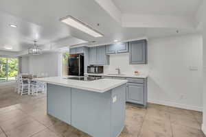 Kitchen featuring a raised ceiling, black appliances, gray cabinetry, light countertops, and recessed lighting