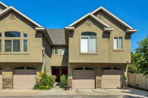 View of front of home featuring a garage, stucco siding, stone siding, and driveway
