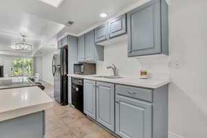 Kitchen featuring black appliances, gray cabinets, light countertops, and decorative light fixtures
