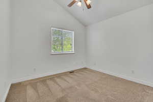 Empty room with carpet, a ceiling fan, and vaulted ceiling