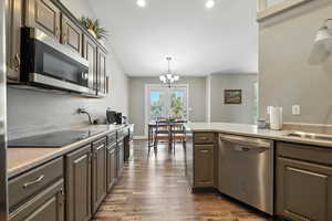 Kitchen featuring appliances with stainless steel finishes, a chandelier, light countertops, dark wood-style flooring, and decorative light fixtures