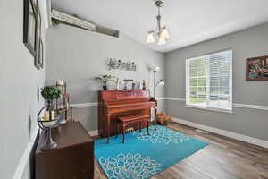 Living area with wood finished floors, a chandelier, and vaulted ceiling