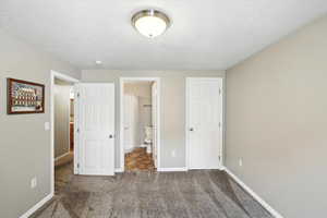 Unfurnished bedroom featuring carpet floors, a textured ceiling, and ensuite bath