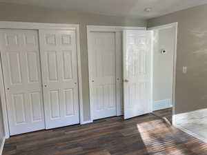 Unfurnished bedroom with two closets and dark wood-type flooring