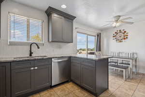 Kitchen with stainless steel dishwasher, a peninsula, backsplash, gray cabinets, and ceiling fan