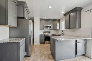 Kitchen with stainless steel appliances, a peninsula, gray cabinetry, tasteful backsplash, and light stone counters