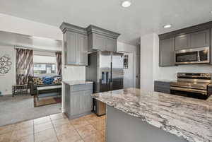 Kitchen with stainless steel appliances, gray cabinetry, light stone counters, light carpet, and recessed lighting