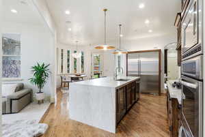 Kitchen featuring built in appliances, light stone countertops, light wood finished floors, decorative light fixtures, and wine cooler