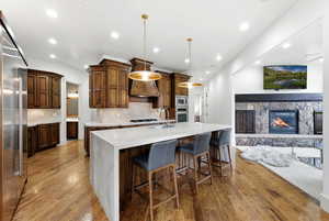Kitchen featuring light stone countertops, decorative light fixtures, a spacious island, built in appliances, and light wood finished floors