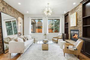 Living area with built in shelves, wood finished floors, a large fireplace, a chandelier, and healthy amount of natural light