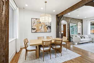 Dining space with a chandelier, light wood-style flooring, beamed ceiling, arched walkways, and recessed lighting