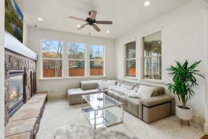 Carpeted living room featuring healthy amount of natural light, ceiling fan, a stone fireplace, and recessed lighting