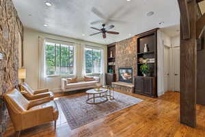 Living room featuring a textured ceiling, built in features, a ceiling fan, a fireplace, and wood finished floors