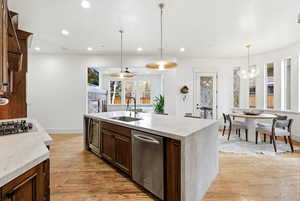 Kitchen featuring dark brown cabinets, light stone counters, an island with sink, appliances with stainless steel finishes, and decorative light fixtures