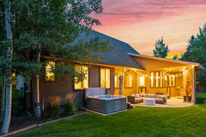 Back of property at dusk with an outdoor living space, a patio, a lawn, a hot tub, and a shingled roof