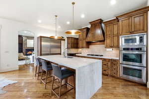 Kitchen featuring brown cabinetry, a kitchen breakfast bar, tasteful backsplash, built in appliances, and hanging light fixtures