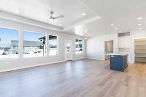Unfurnished living room with ceiling fan, recessed lighting, light wood-style floors, and a tray ceiling