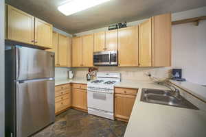 Kitchen with appliances with stainless steel finishes, dark stone finish floors, light brown cabinetry, and light countertops