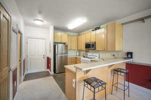 Kitchen featuring appliances with stainless steel finishes, light brown cabinetry, a peninsula, a kitchen breakfast bar, and light countertops