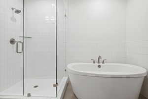 Bathroom with a shower stall, a soaking tub, and tile walls