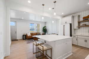 Kitchen with freestanding refrigerator, backsplash, open shelves, light wood-style floors, and light countertops