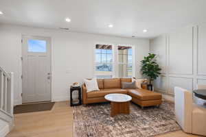 Living room featuring light wood-style floors, plenty of natural light, a decorative wall, recessed lighting, and stairway