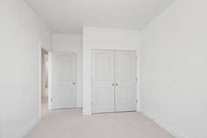 Unfurnished bedroom with light carpet and a closet
