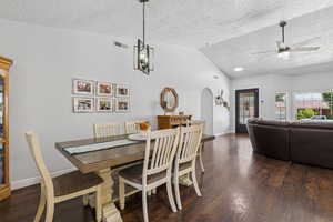 Dining room with a textured ceiling, vaulted ceiling, arched walkways, a ceiling fan, and dark wood-type flooring