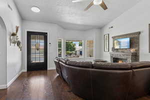 Living area with a fireplace, ceiling fan, dark wood-style floors, arched walkways, and a textured ceiling