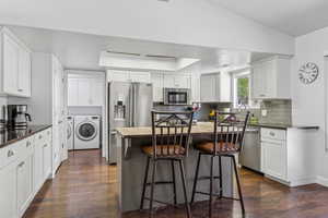 Kitchen featuring appliances with stainless steel finishes, independent washer and dryer, dark wood finished floors, and backsplash