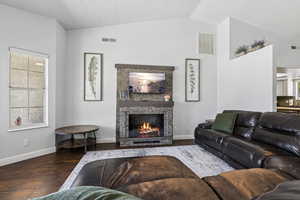 Living room with vaulted ceiling, wood finished floors, and a fireplace