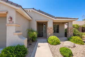 Doorway to property with stucco siding, stone siding, a porch, and a tile roof