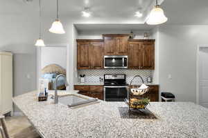 Kitchen with appliances with stainless steel finishes, backsplash, pendant lighting, and light stone countertops