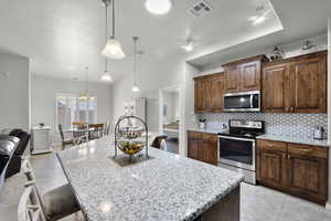 Kitchen featuring appliances with stainless steel finishes, backsplash, a kitchen island, light stone counters, and ceiling fan