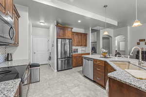 Kitchen featuring appliances with stainless steel finishes, arched walkways, backsplash, decorative light fixtures, and light tile patterned floors