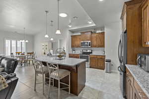 Kitchen with appliances with stainless steel finishes, brown cabinetry, tasteful backsplash, light tile patterned floors, and a kitchen breakfast bar
