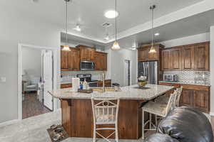Kitchen featuring appliances with stainless steel finishes, a tray ceiling, a kitchen breakfast bar, decorative backsplash, and light stone countertops
