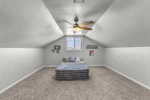 Carpeted bedroom featuring a textured ceiling, ceiling fan, and vaulted ceiling