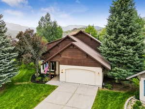 View of front of house featuring a mountain view, a front lawn, driveway, stucco siding, and a garage