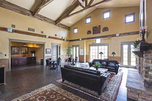 Living room featuring high vaulted ceiling, beamed ceiling, healthy amount of natural light, and dark stone finish floors