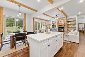 Kitchen featuring a fireplace, dark wood-style floors, beamed ceiling, ceiling fan, and white cabinetry