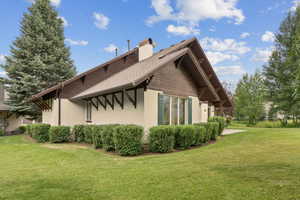 View of side of home featuring a chimney, a yard, stucco siding, and roof with shingles