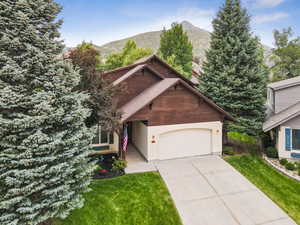 View of front of house with a garage, a front yard, stucco siding, a mountain view, and driveway